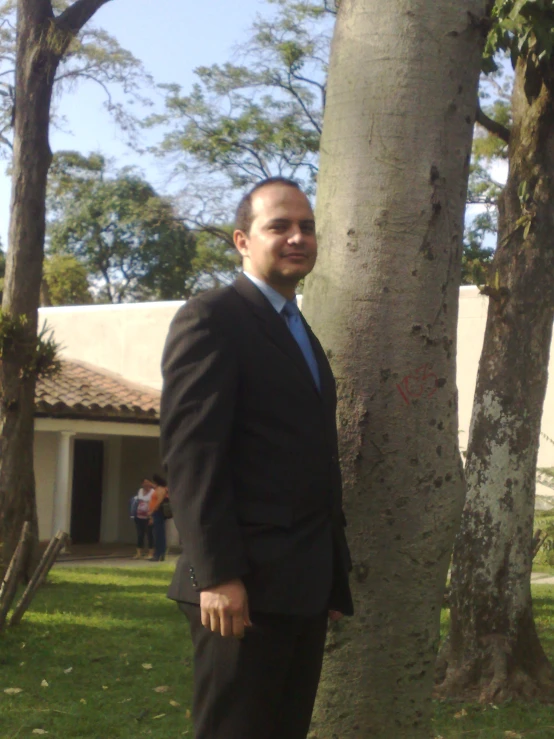 a man in a business suit and tie leans against a tree