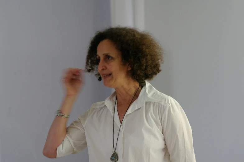 a woman wearing a necklace and shirt standing in front of a wall