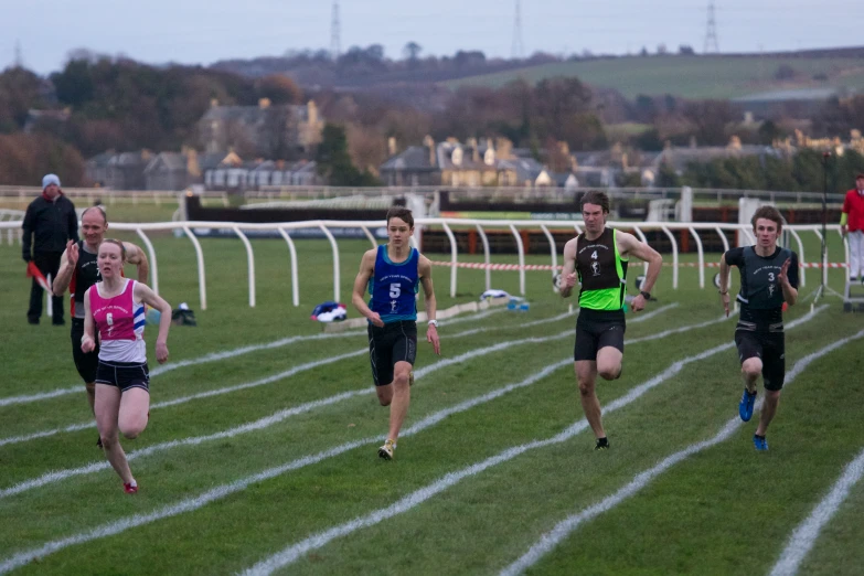 runners in athletic uniforms racing on a grass track
