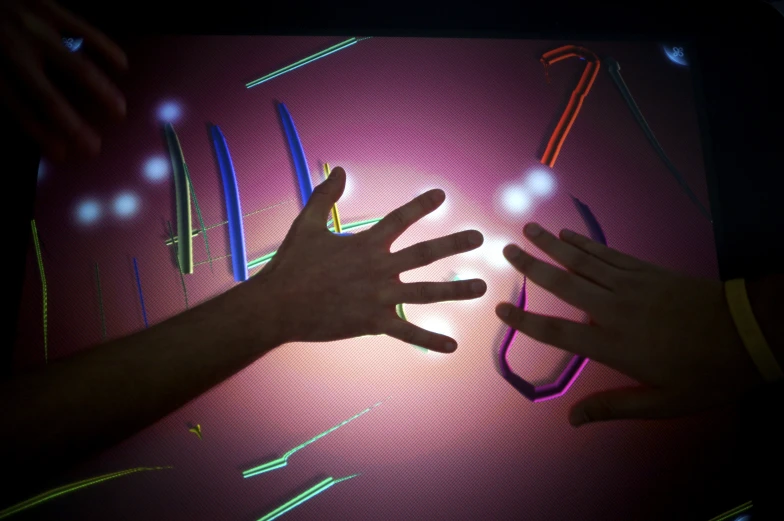 person reaching up towards colorful lights with their hands