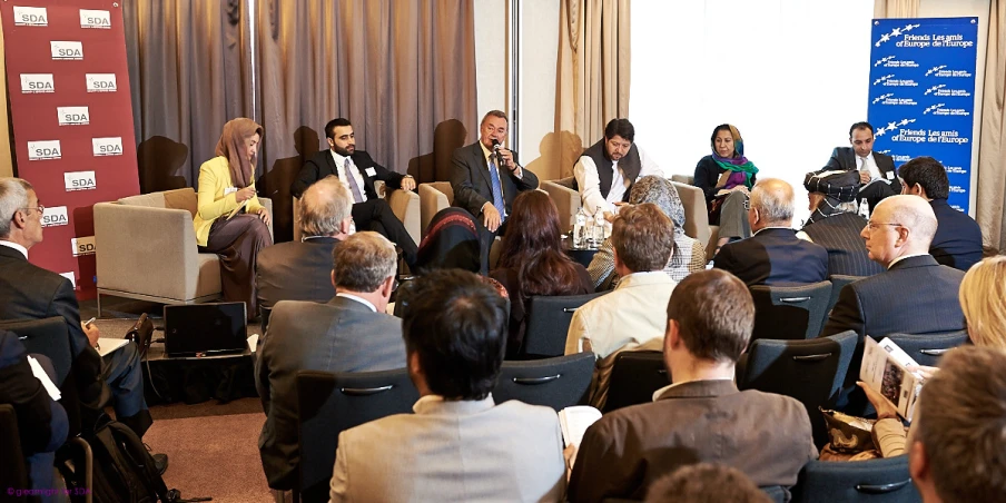 an audience of people sitting in chairs with a man giving a speech