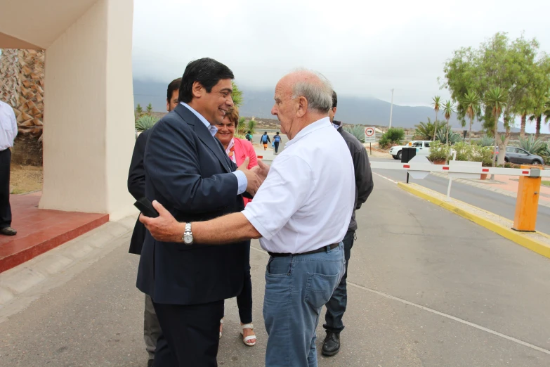 two men shake hands in a parking lot near others