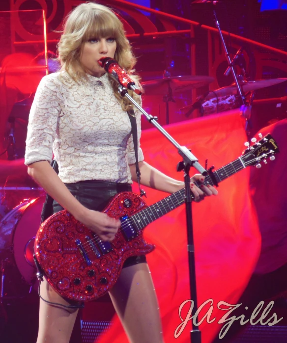 a woman with a red guitar is singing in front of a microphone