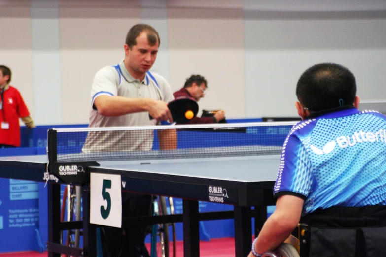 two men play table tennis in an indoor ping pong match