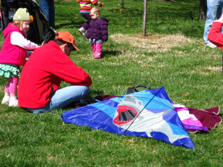 two people kneeling next to a child with a kite on a field