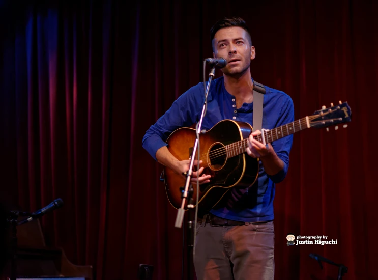 a man in blue shirt playing guitar in front of microphone