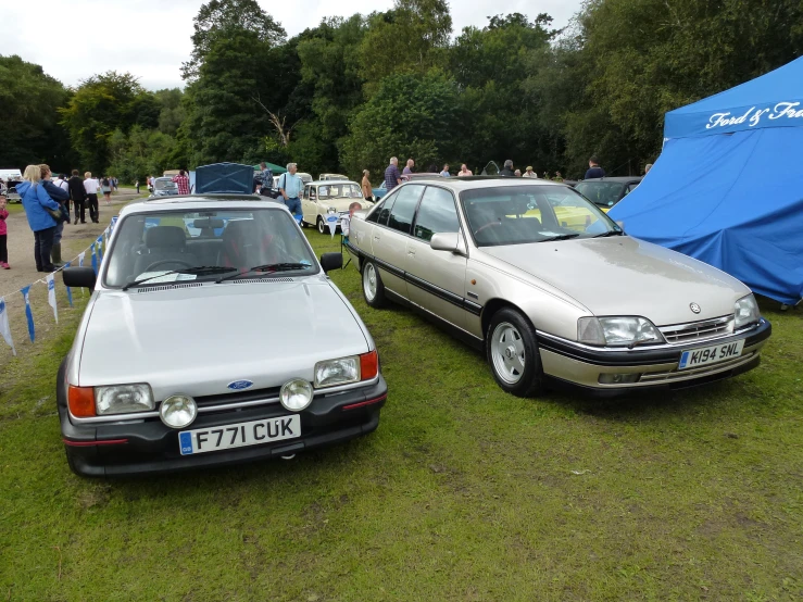 two cars are parked on the grass with a blue tent