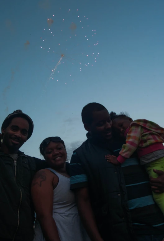 three people standing next to each other with a group of fireworks in the sky above them