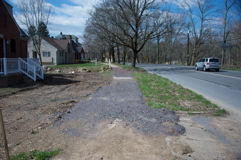 a dirt driveway with little grass on top next to a house