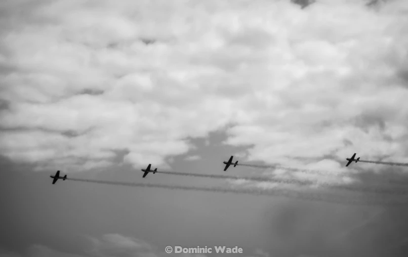 four planes flying through a cloudy sky with contrails