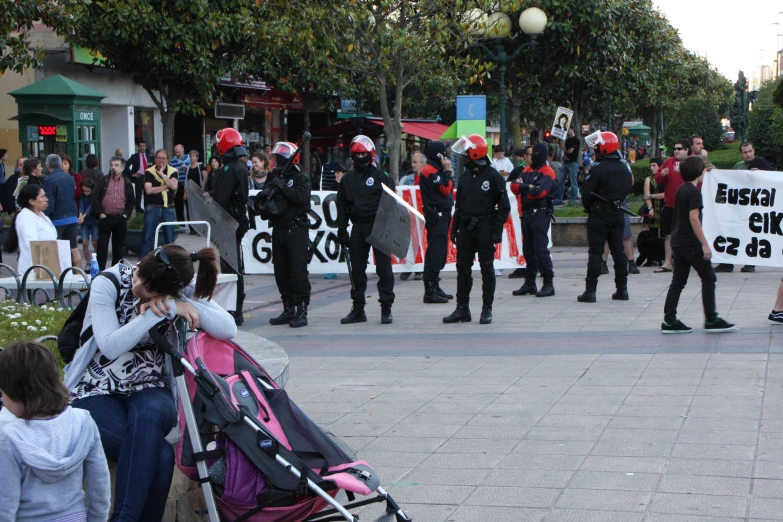 a group of protesters in black jackets and with red hats, sit in front of a street