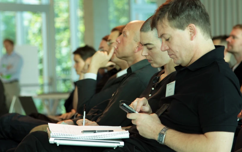 three men sitting in front of a crowd, looking at their cellphones