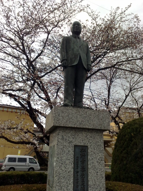 statue of a man in coat sitting on cement base with a car nearby