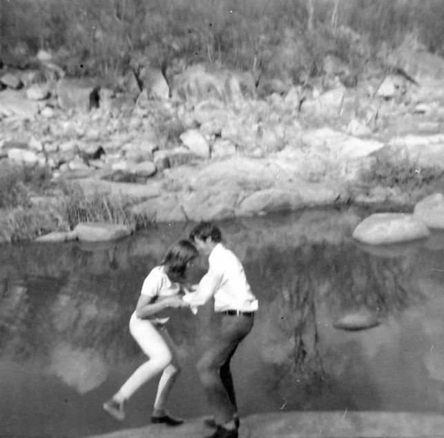 black and white image of two people dancing next to a river