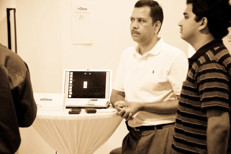 three men are gathered around and one is on his computer