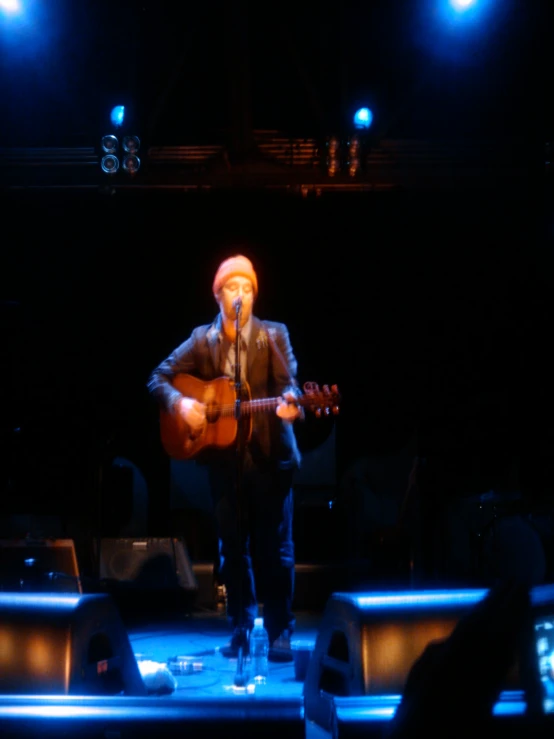 a man with a hat and necktie playing a guitar on stage