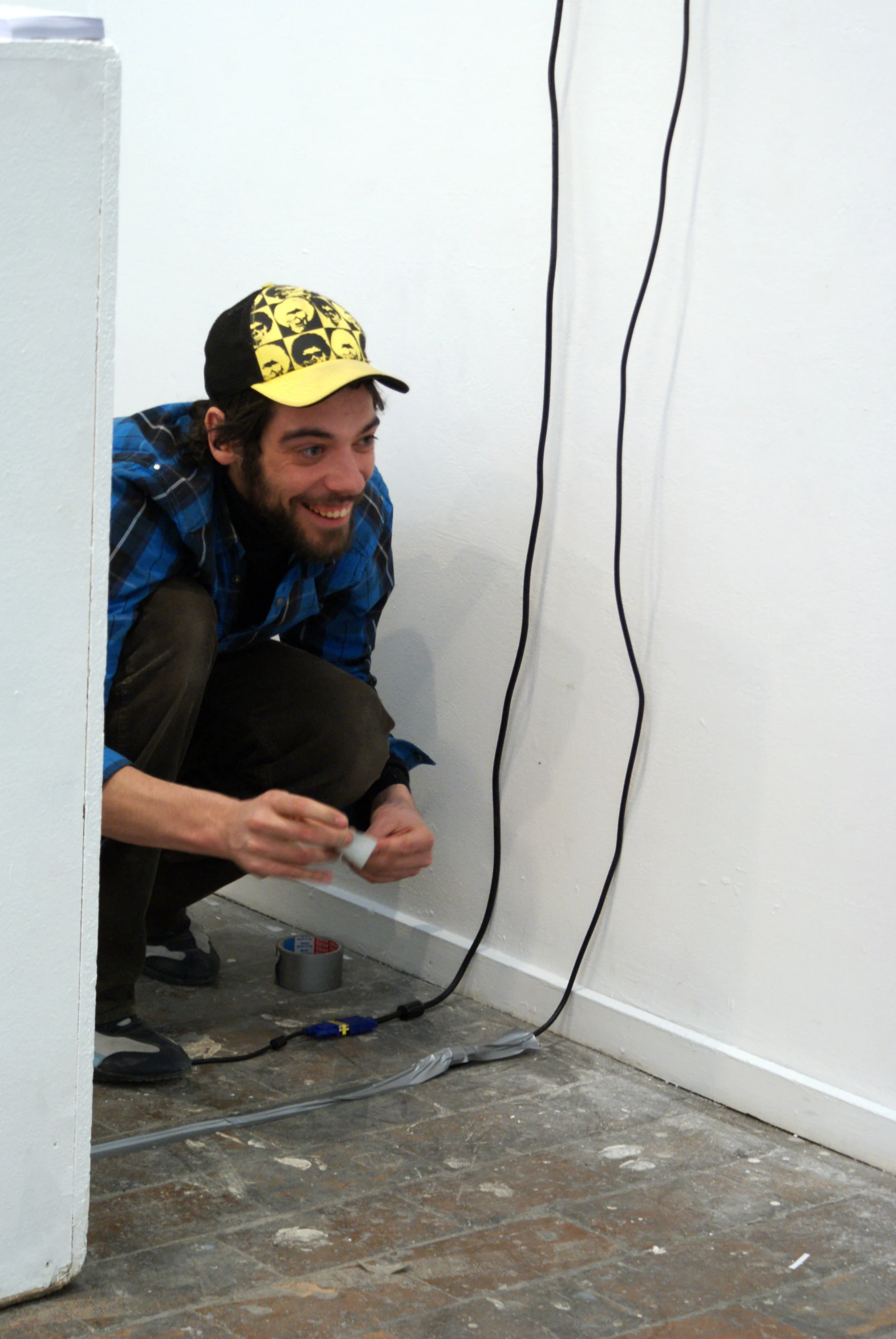 a man wearing a yellow hat crouches down in front of an electrical outlet