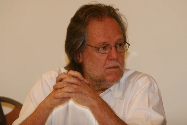 an older man sitting at his desk with his hands clasped