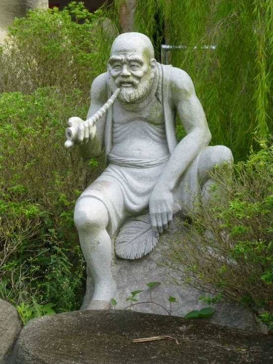 an old statue sitting on top of a rock in front of some bushes