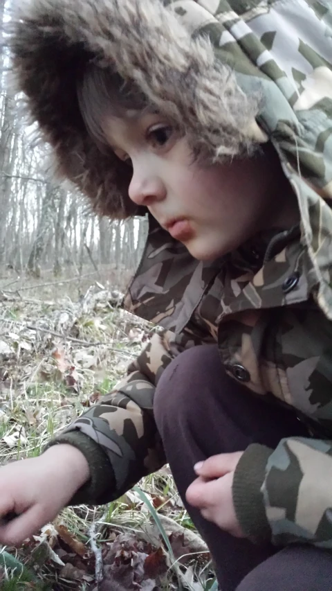 a child sits on the ground in the woods wearing a jacket