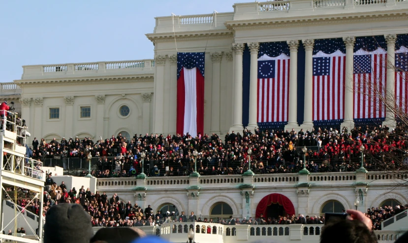 many people are in a large building with two huge american flags on the balcony