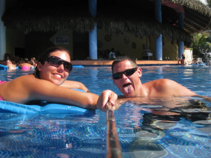 a couple with sunglasses taking selfies in an outdoor pool