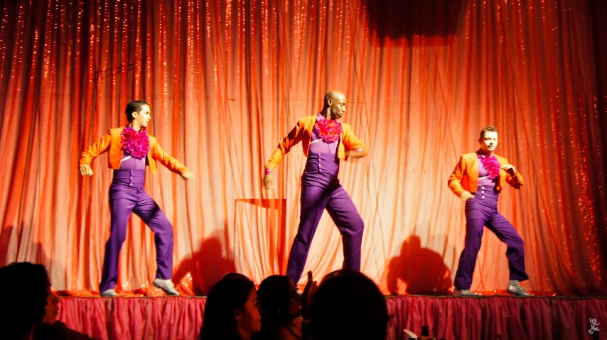 three performers on stage with an audience watching