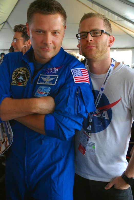 two men, one with an american flag and another in blue, are looking at the camera