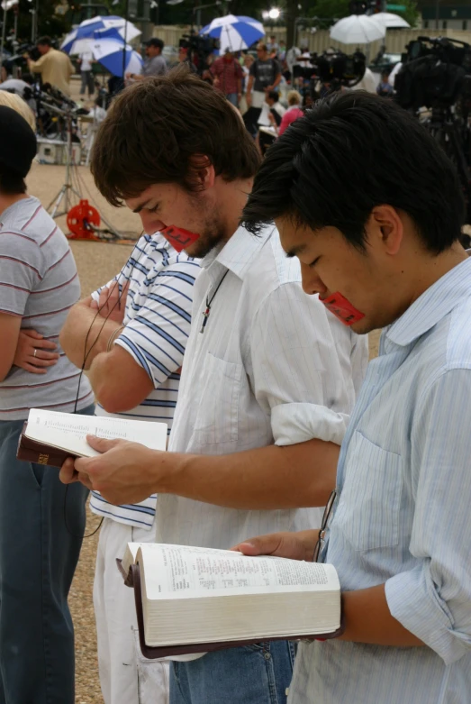 three men look at an open book as people stand in the background