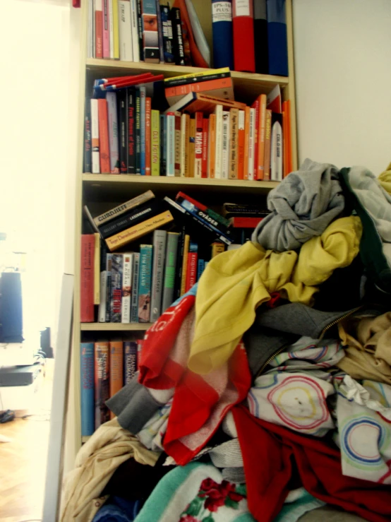 books are piled on top of a bed and several other things to put in the bookcase