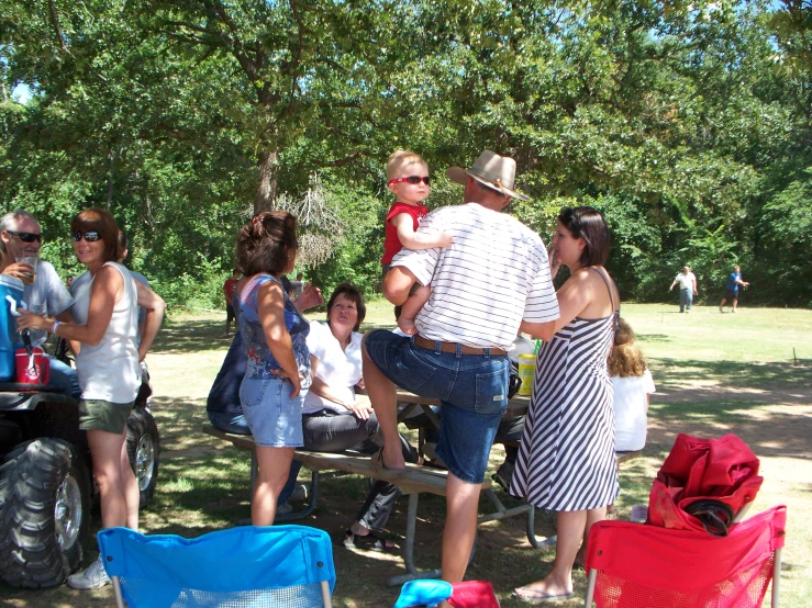 people gathered outside around a picnic table with a large tractor in the background