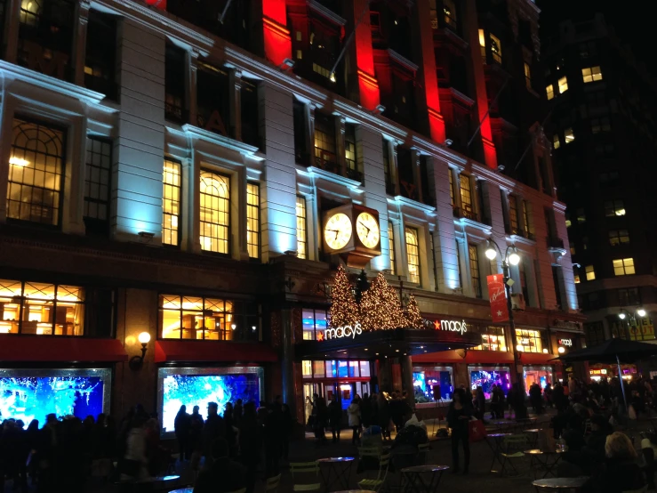 many people are standing on the street in front of buildings with decorated christmas trees