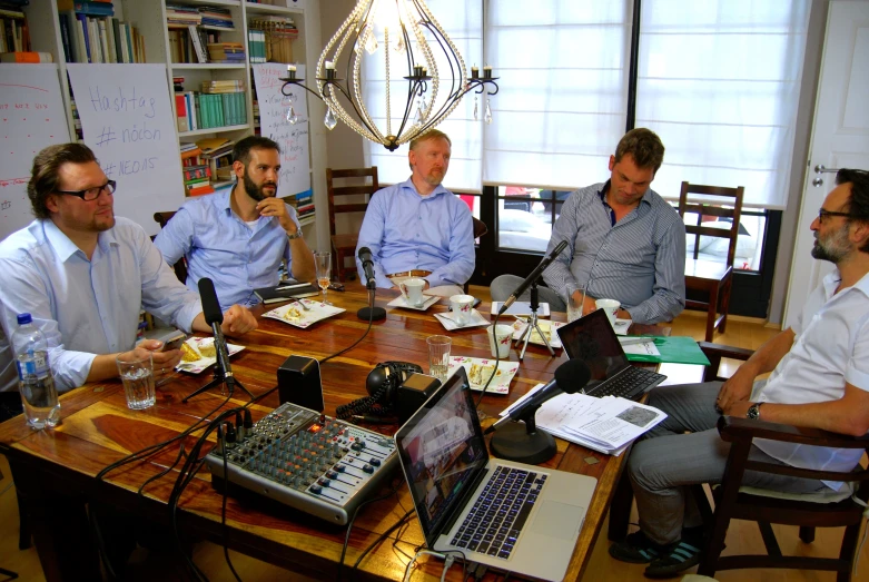 five men sit around a table listening to the sound of their laptop