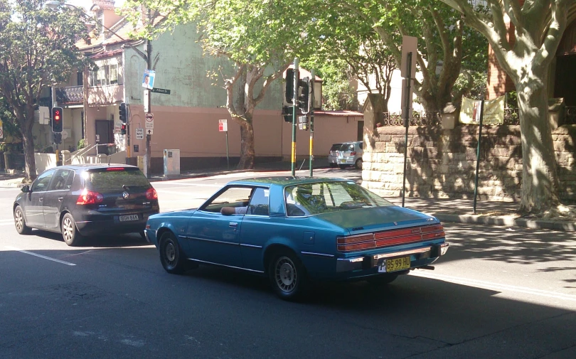 the blue car is moving along the tree - lined street