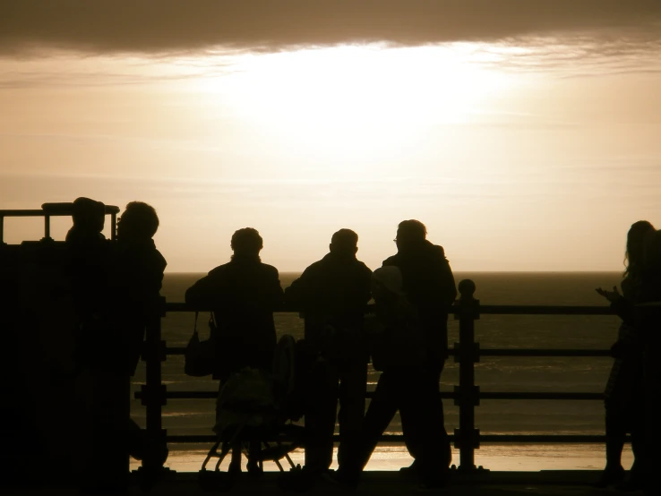 some people standing next to the ocean under a setting sun