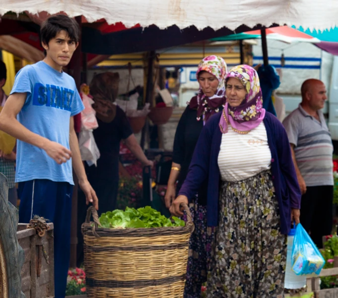 a woman walking around a farmers market holding a basket of lettuce