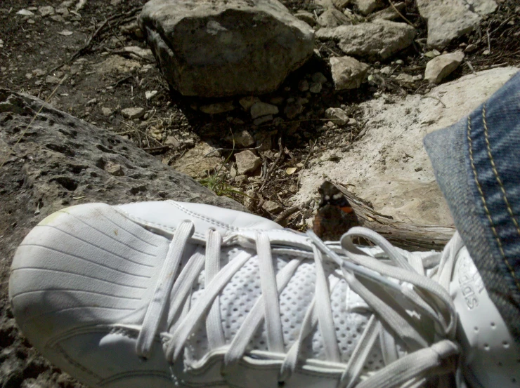 someone's white tennis shoes standing on rocky ground