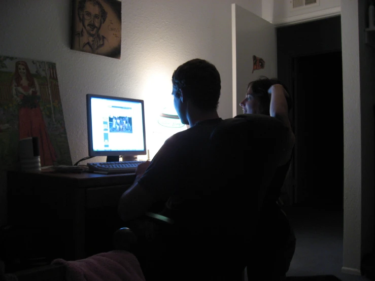 a man in the dark looking at a computer monitor