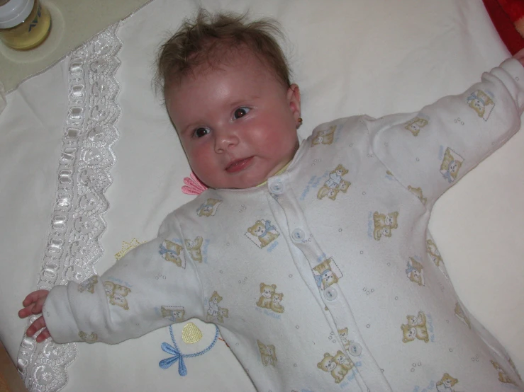 a baby laying on a white blanket holding her hand up