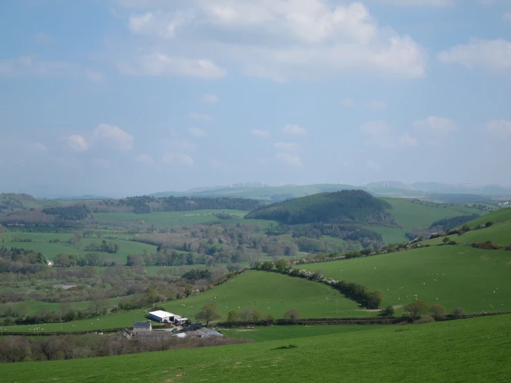 a green hillside surrounded by hills and a barn