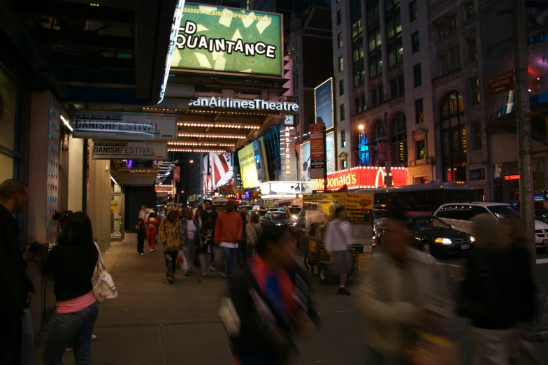 people walking on a sidewalk under the illuminated entrance of a building