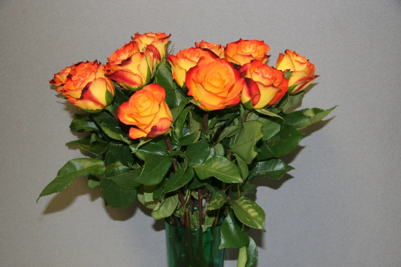 orange roses in a green vase sitting on a table