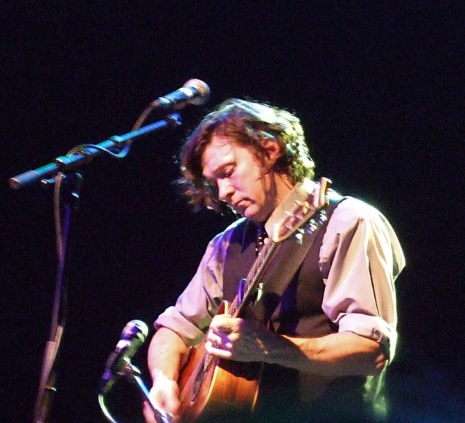 a man with a guitar standing in front of a microphone