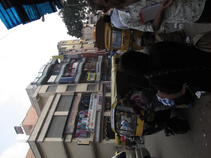 people walk down a crowded street lined with parked auto rickshaws