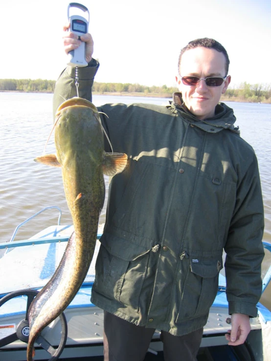 man holding up his large fish with a cell phone