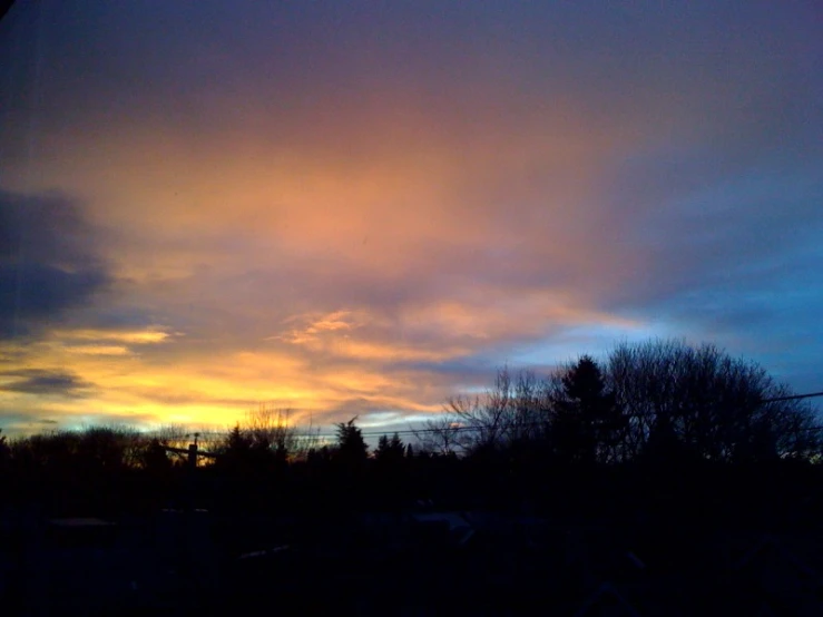 the sky is beautiful at sunset with trees in front