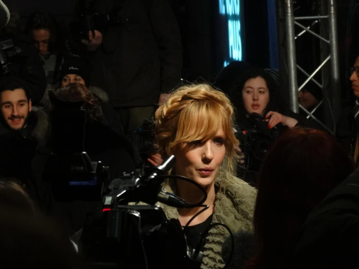 the red headed woman is behind a camera in front of a group of people