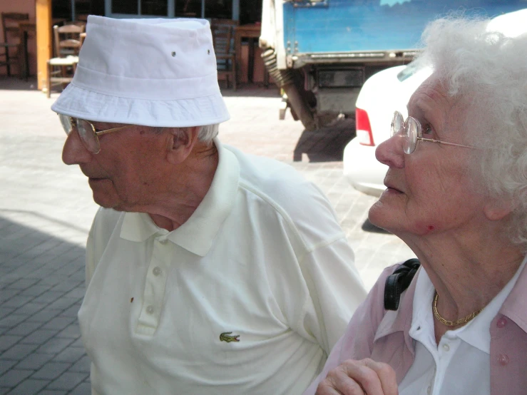 an old couple wearing white hats on a street