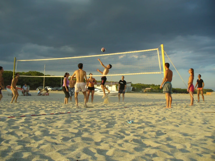 a group of people are standing on the sand near a volley ball net