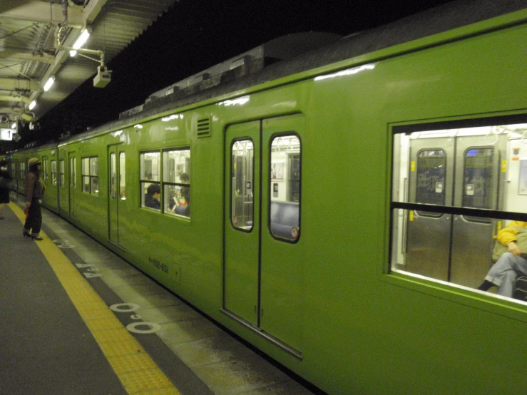 people standing outside the green train stopped at the platform